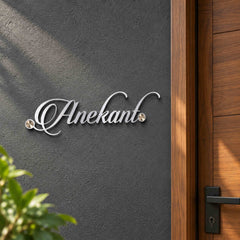 Anekant silver-tone script nameplate shown installed on a charcoal wall beside a walnut apartment entrance door