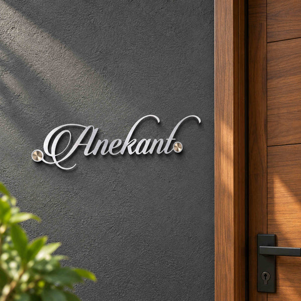 Anekant silver-tone script nameplate shown installed on a charcoal wall beside a walnut apartment entrance door