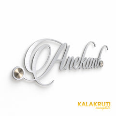 Anekant silver-tone script nameplate from the left, showing the thin cut-out lettering and mounting caps