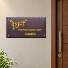 Engraved brown stone family nameplate with golden Devanagari lettering, installed level beside an apartment door