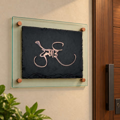 Desai black stone and antique copper nameplate with green-tinted glass backing, shown installed beside an apartment entrance
