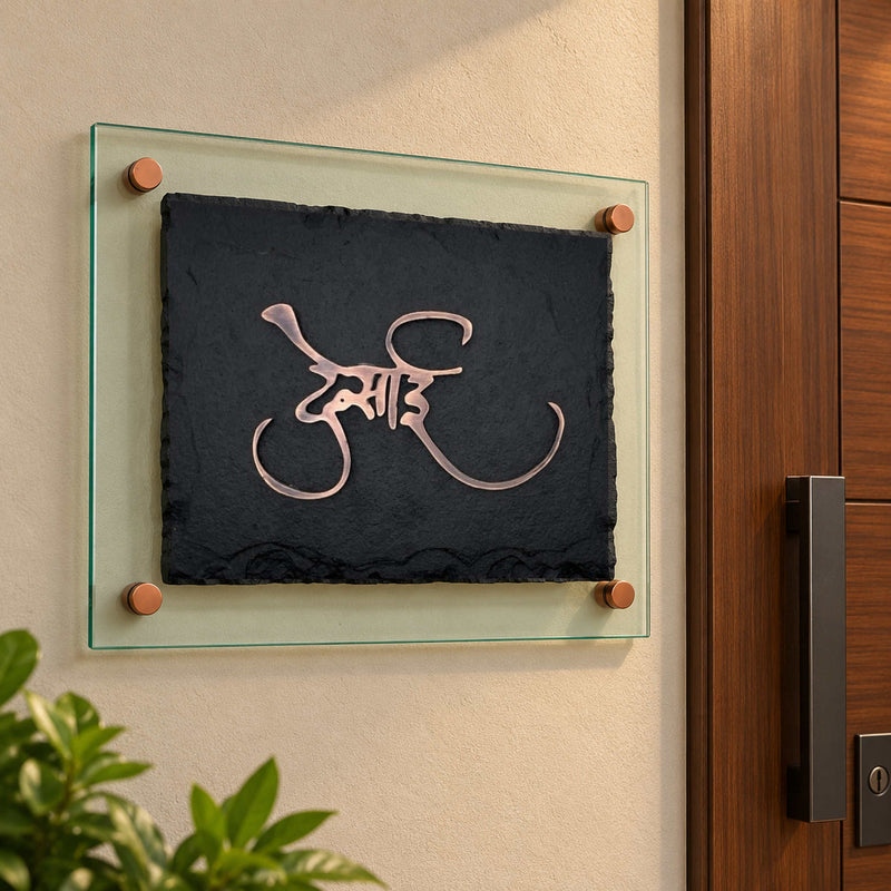 Desai black stone and antique copper nameplate with green-tinted glass backing, shown installed beside an apartment entrance