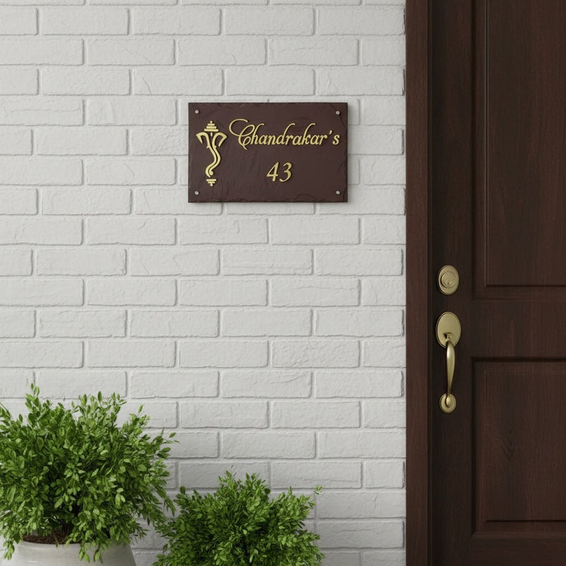 Chandrakar brown stone and brass nameplate shown installed on a white brick wall beside a timber entrance door