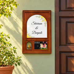 Shriram and Deepali floral wooden nameplate with hanging bell and B-804 cow artwork on a sage-green entrance wall.